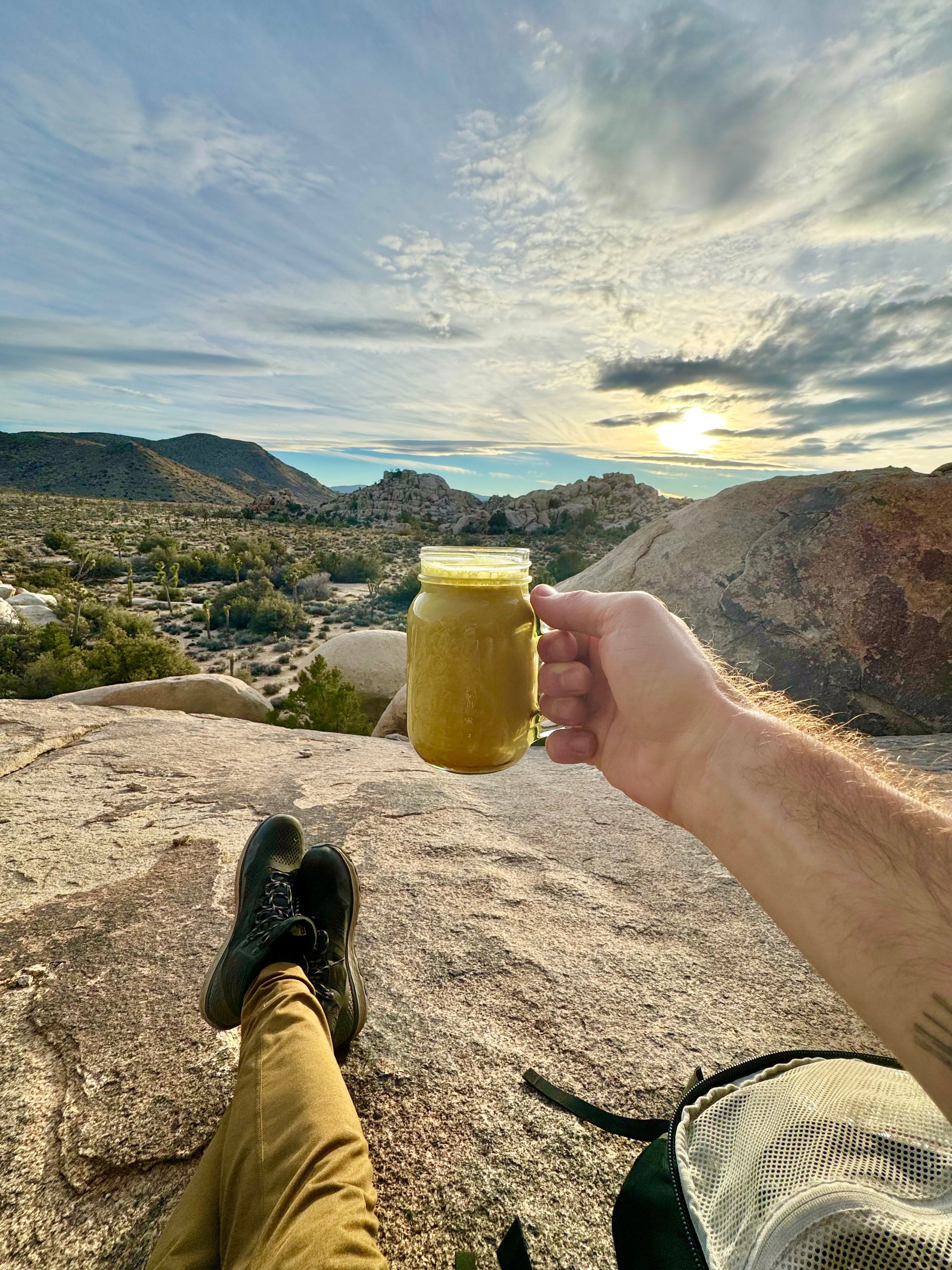 Person holding a cup of turmeric latte made with Good Day Latte with a scenic view of mountains and sky in the background