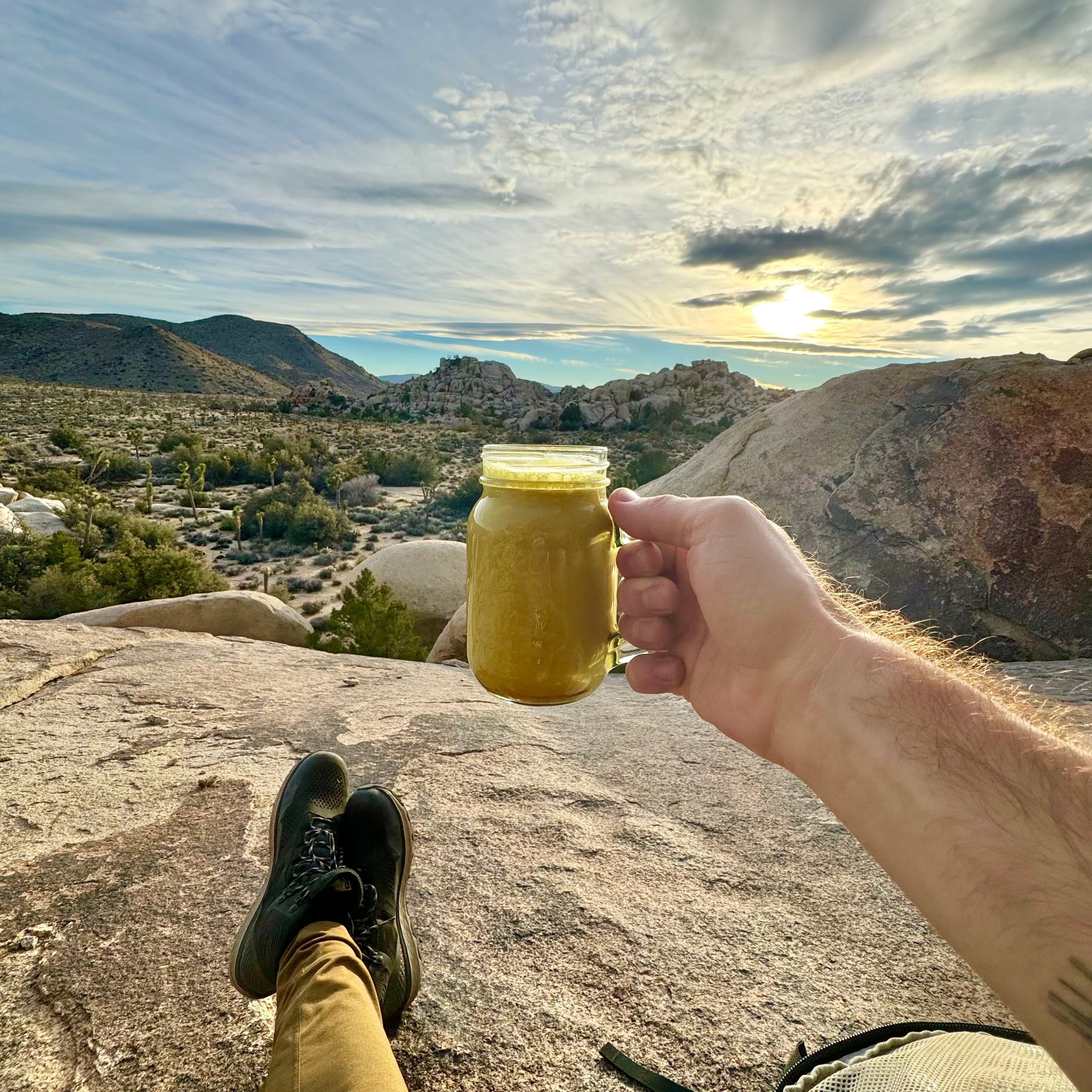 Person holding a cup of turmeric latte made with Good Day Latte with a scenic view of mountains and sky in the background