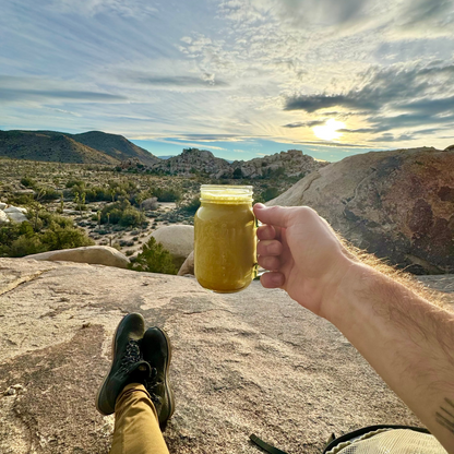 Person holding a cup of turmeric latte made with Good Day Latte with a scenic view of mountains and sky in the background
